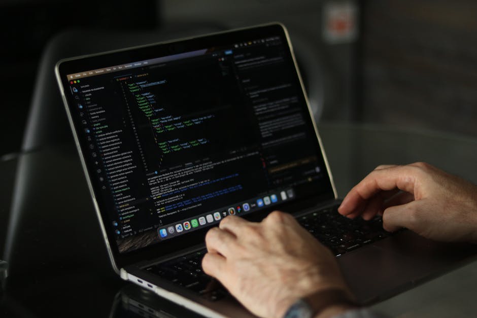A close-up view of a pink MacBook Air laptop computer displaying lines of colorful code on its screen, set against a blurred warm-orange background. The screen shows syntax-highlighted text with vario